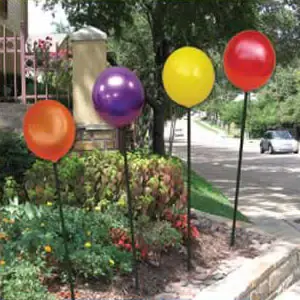 Colorful balloons on sticks by roadside garden.