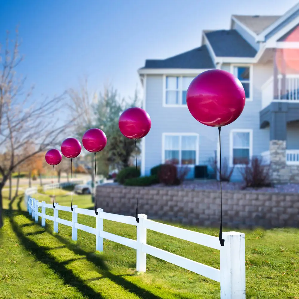 Red balloons on a white picket fence.